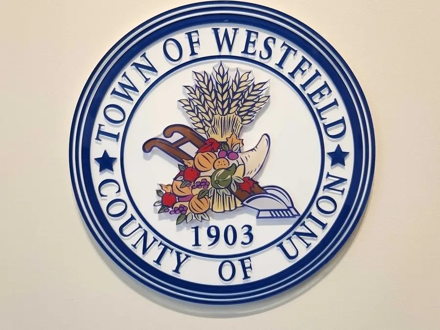 own of Westfield official seal mounted on a wall, featuring a blue circular emblem with the words “Town of Westfield, County of Union” surrounding a cornucopia and wheat design with the year 1903.