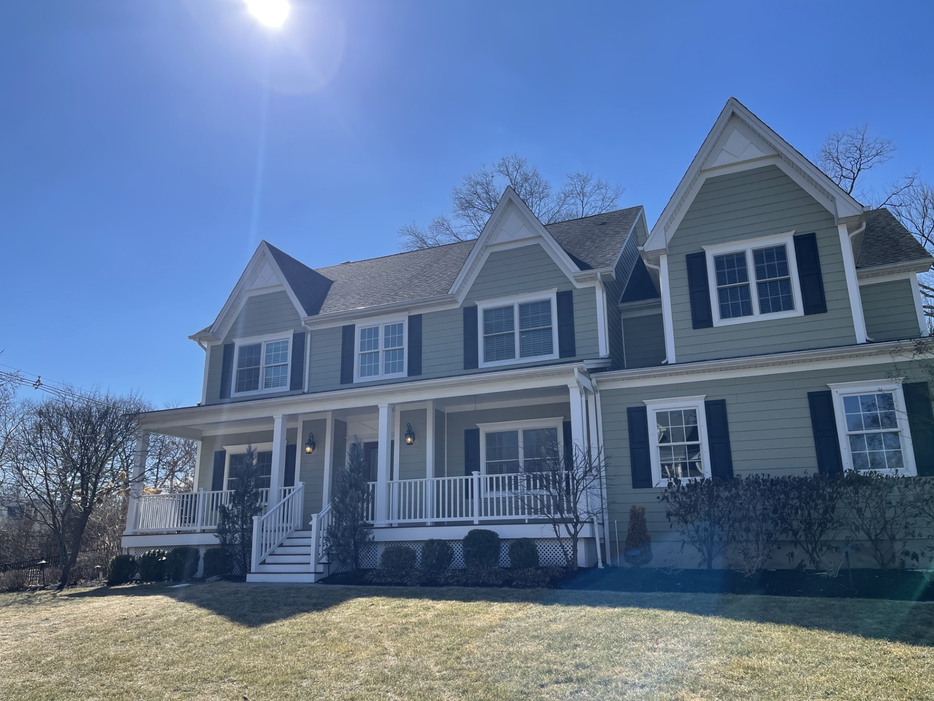 Large custom Colonial-style home in Scotch Plains, New Jersey featuring a wraparound front porch, gabled rooflines, manicured landscaping, and spacious front yard on a sunny day.