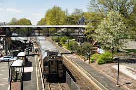 NJ Transit train at Fanwood Station with platforms, a pedestrian bridge, and leafy trees.