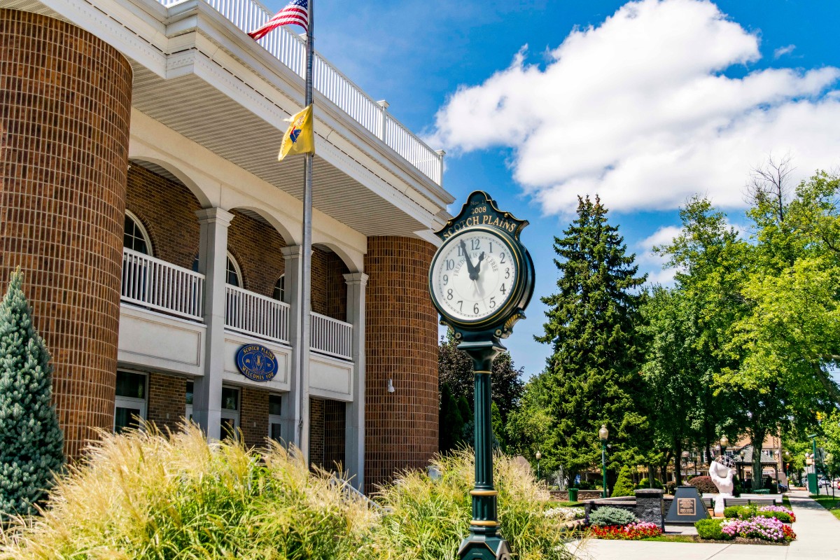 Historic Scotch Plains town clock in front of the municipal building with landscaped gardens and a blue sky.